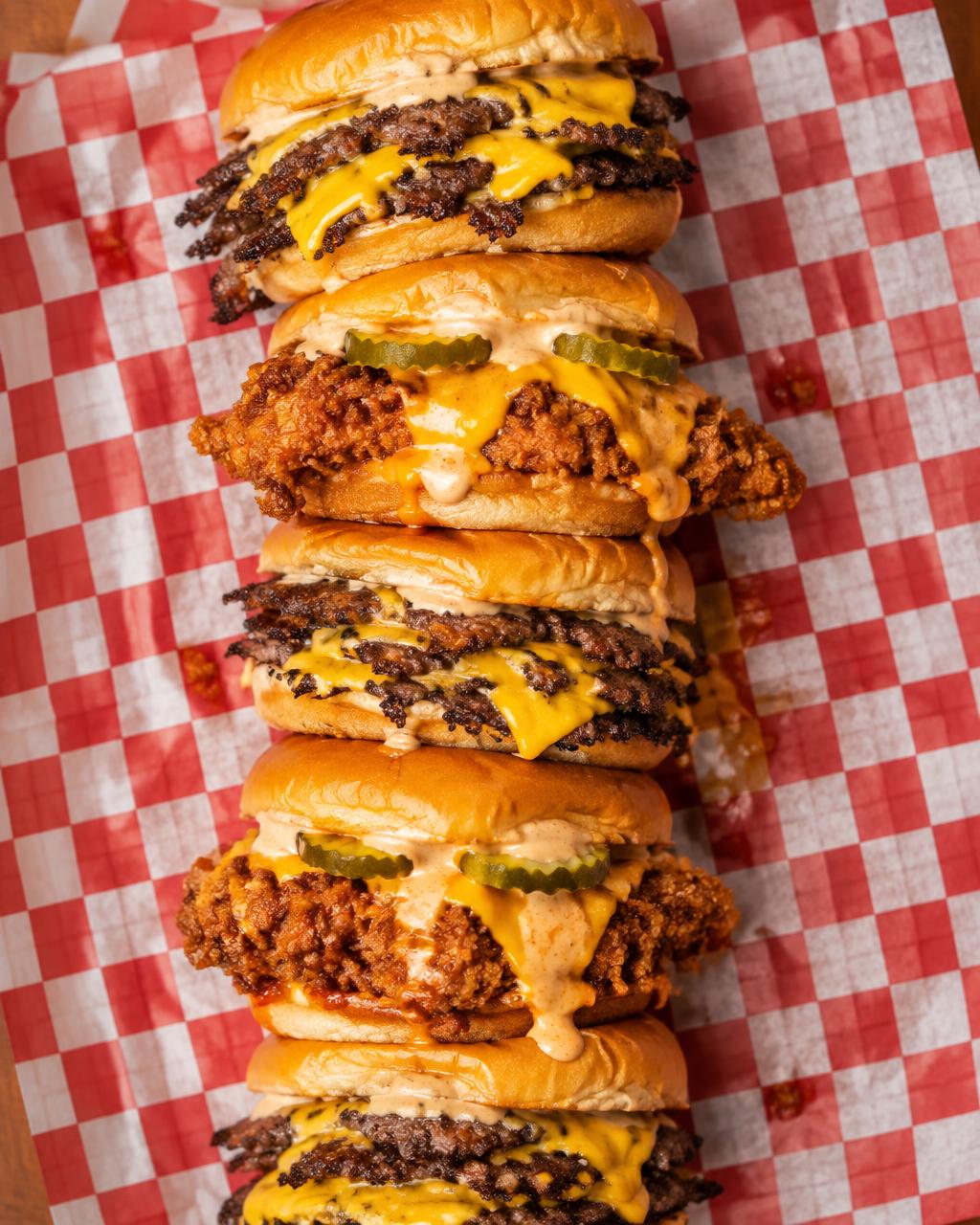 A stack of smash burger and crispy chicken sliders on checkered paper